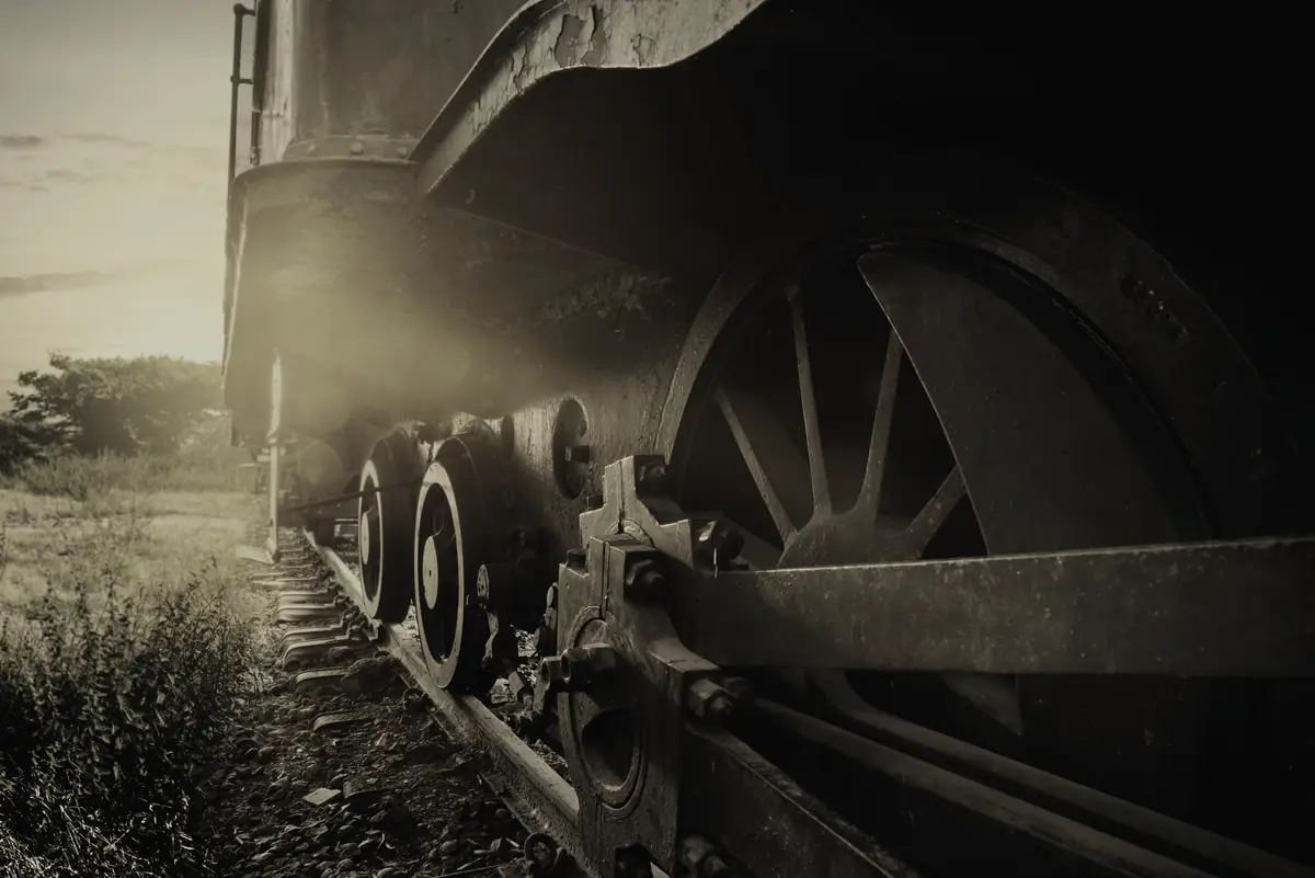 Driving wheels and coupling rod of a standing locomotive, seen low along the rail.
