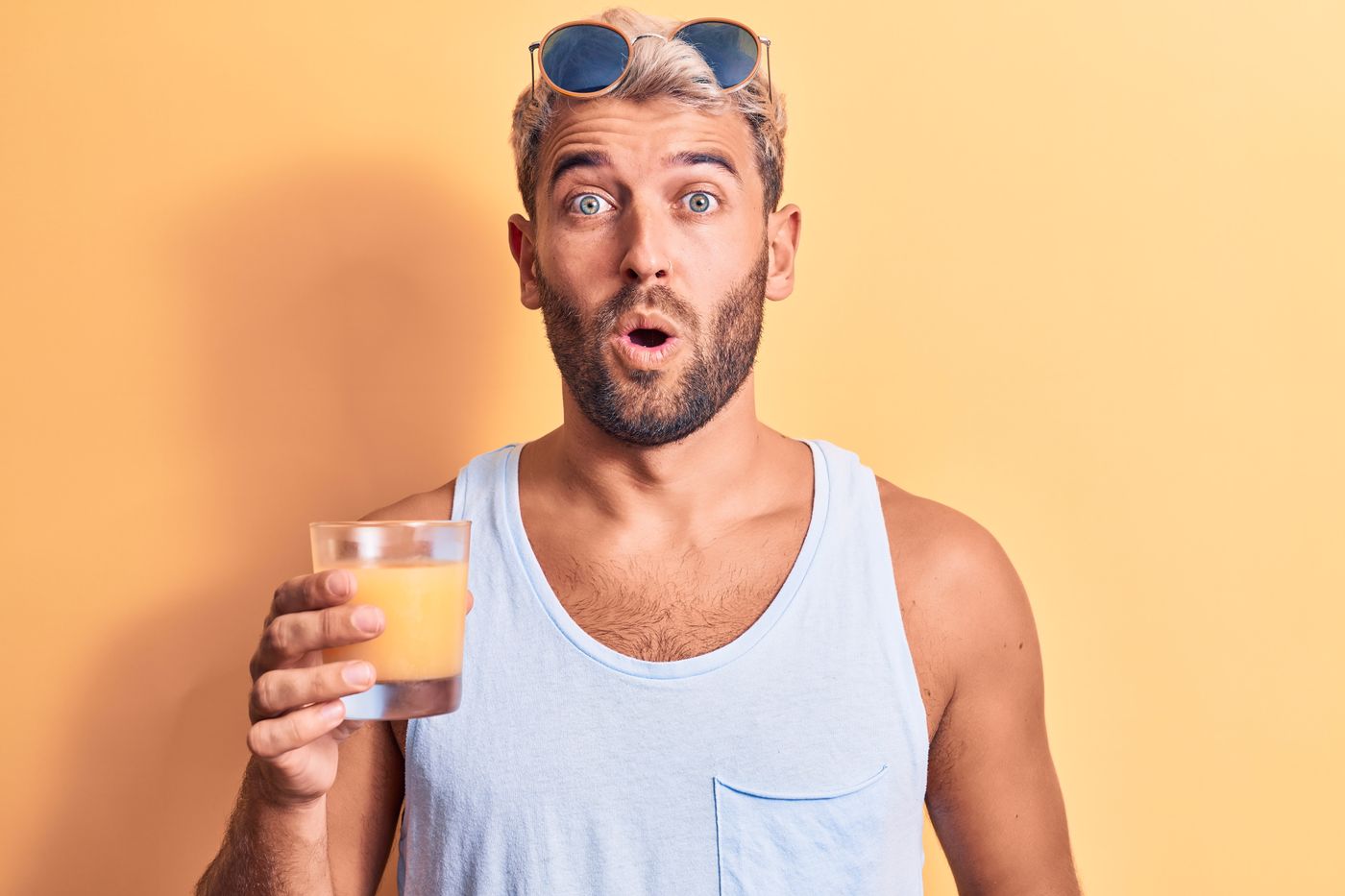 A bearded man in a vest, sunglasses pushed up on his head, holding a glass and staring at the camera with his mouth open.