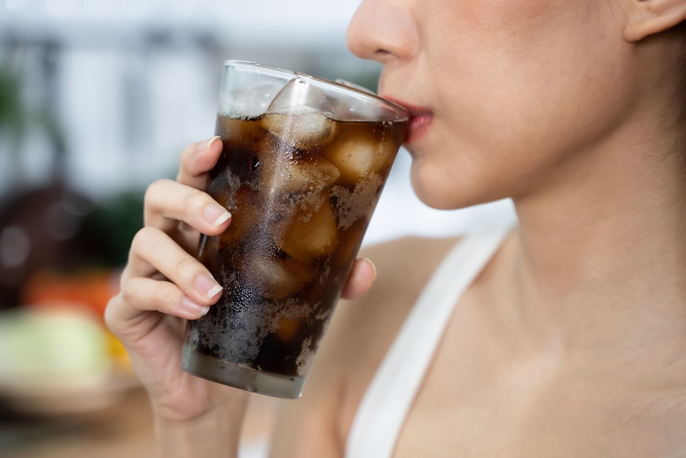 Close crop of a woman drinking from a tall glass full of ice, eyes down, mid-sip.