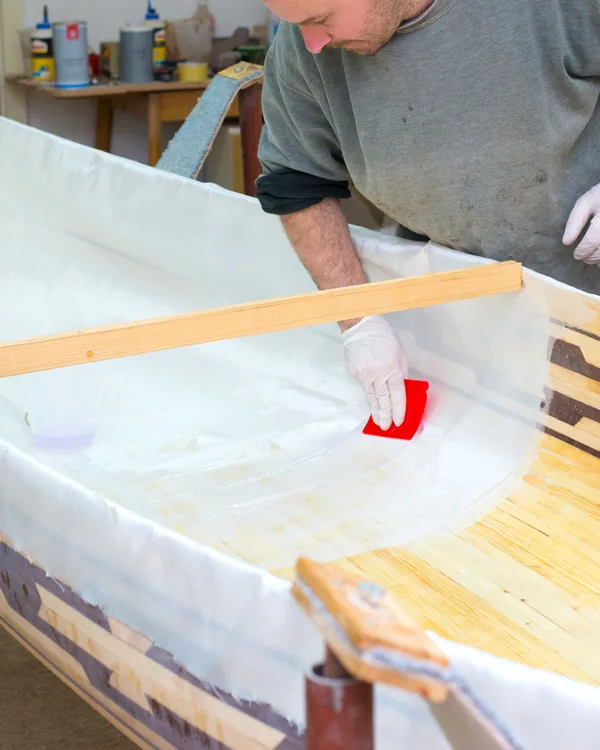 A hull being planked over its bucks in the shed, a builder working a batten along the sheer