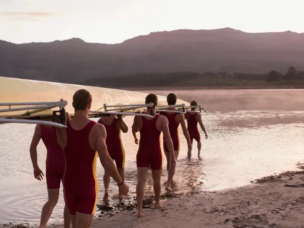 A rowing crew carrying a racing shell into still water at dawn
