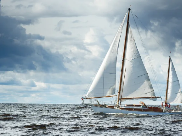 A wooden yawl under sail in open water and grey cloud