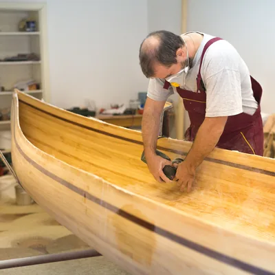 A boatbuilder working along the gunwale of a canoe in the shed