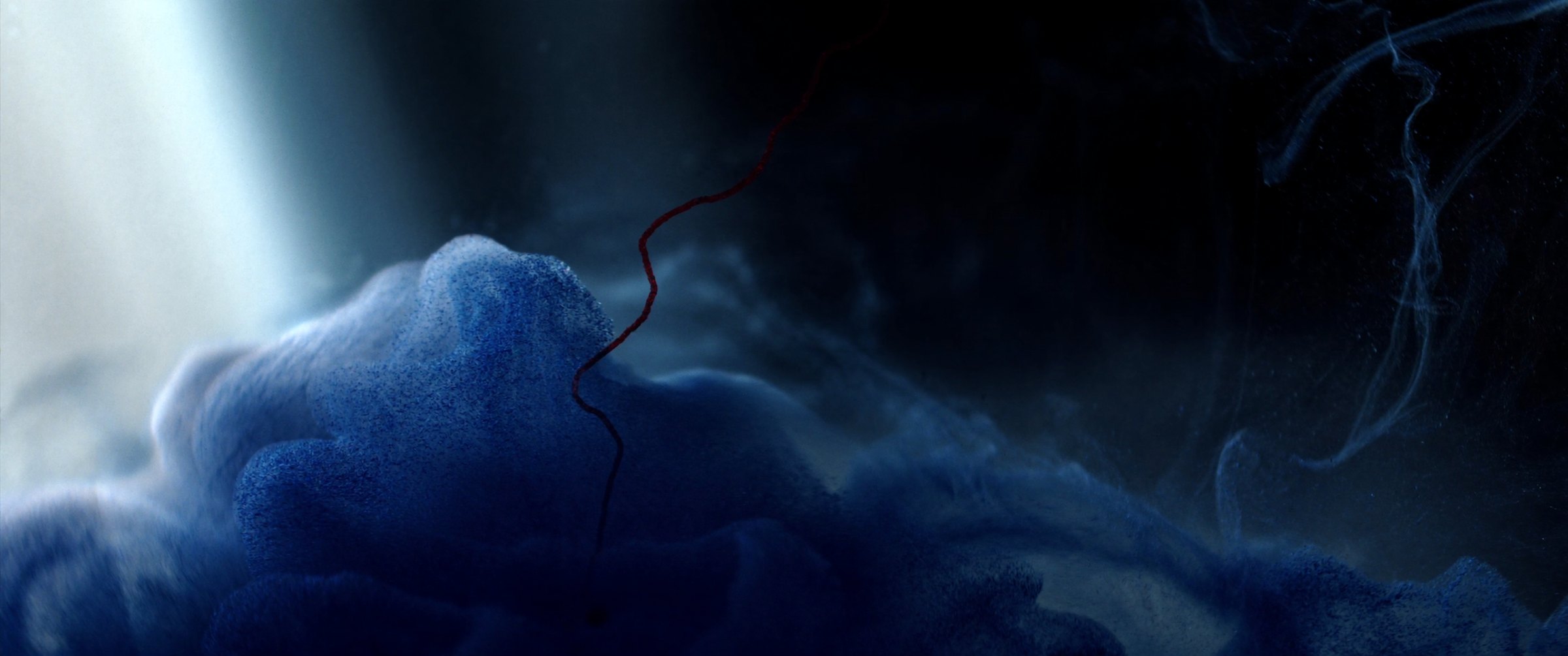 Indigo pigment blooming in water, one madder thread through it