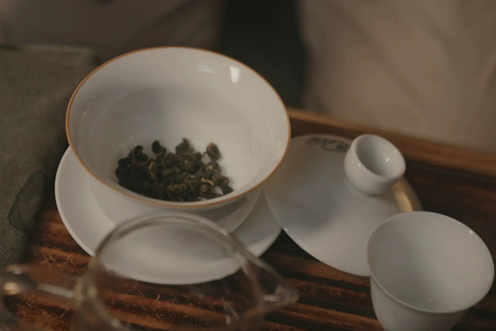 Dry knots of rolled oolong in a warmed white gaiwan, its lid and a small cup beside it on a wooden tea tray