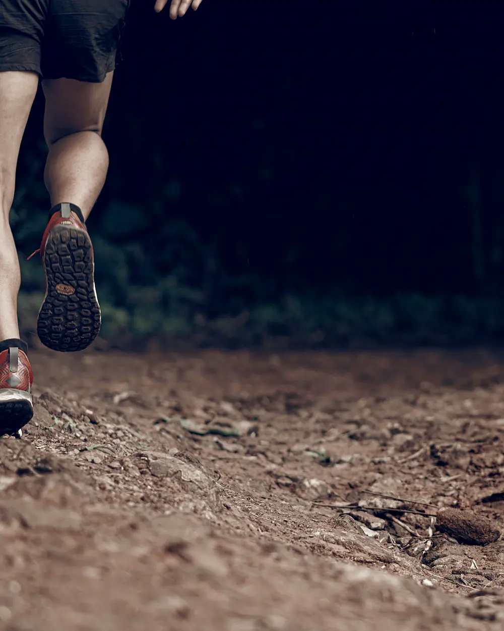 A close view of a runner's legs and shoes mid-stride on a dirt track.