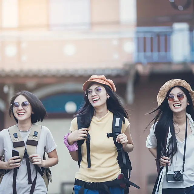 Three travellers laughing as they walk a Kanazawa street with cameras and day bags